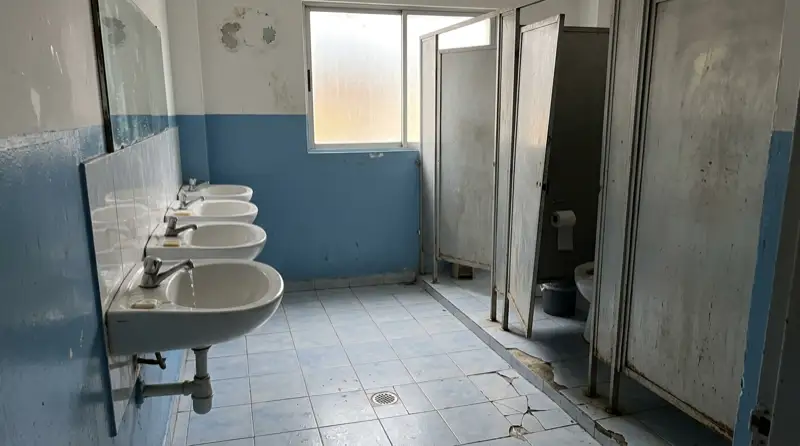 Baño de un colegio público deteriorado: baldosas rotas y paredes manchadas