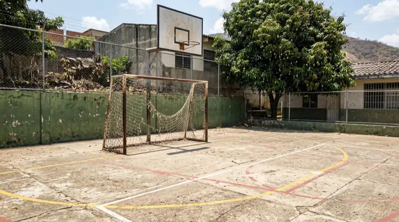 Cancha de un colegio público con el arco oxidado y la malla caída